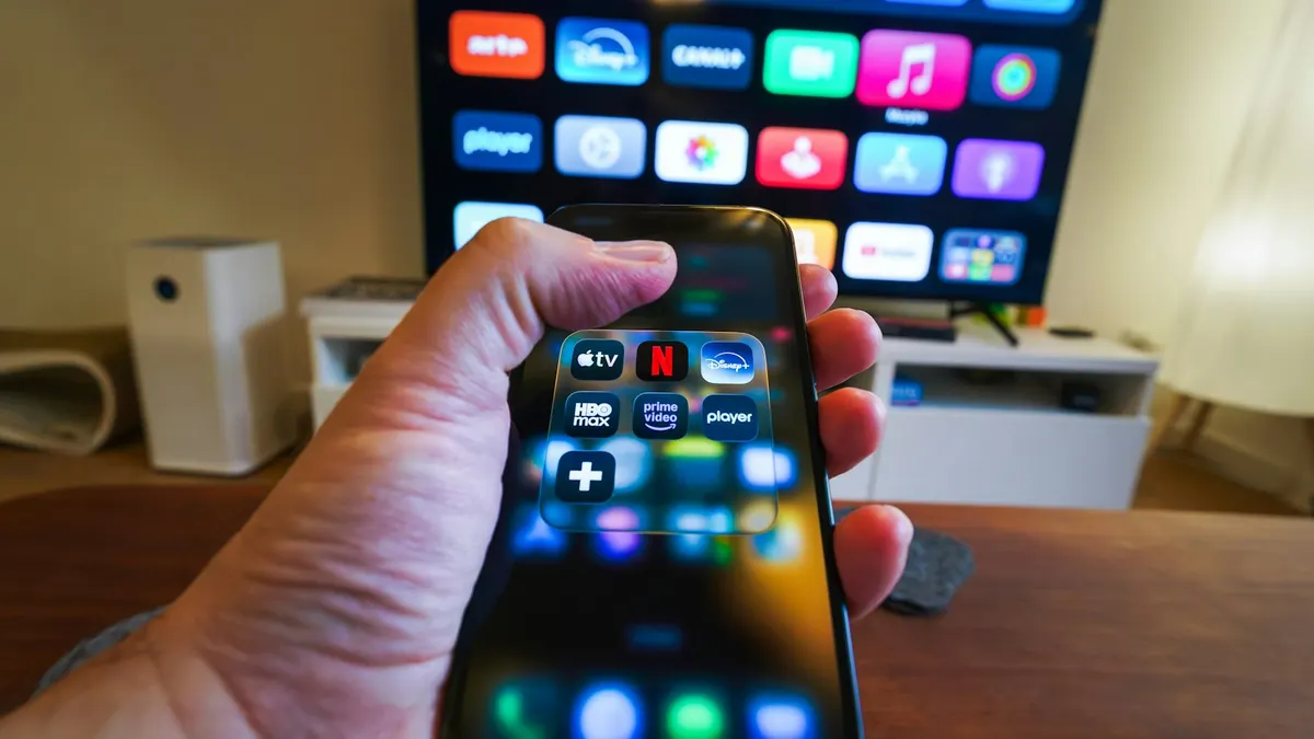 Hand hält ein Smartphone mit einer geöffneten IPTV-App im Wohnzimmer